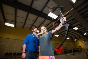 Instructor Matt Brackhan watches Lila Donahoe of Lincoln shoot a bow in the indoor archery range at the Nebraska Outdoor Education Center (NOEC) in Lincoln. Lancaster County. Fowler, June 3, 2015. Copyright NEBRASKAland Magazine, Nebraska Game and Parks Commission.