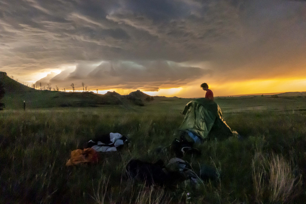 Sawyer Haag sets up a tent in the Pine Ridge at sunset as a storm brews on the horizon.