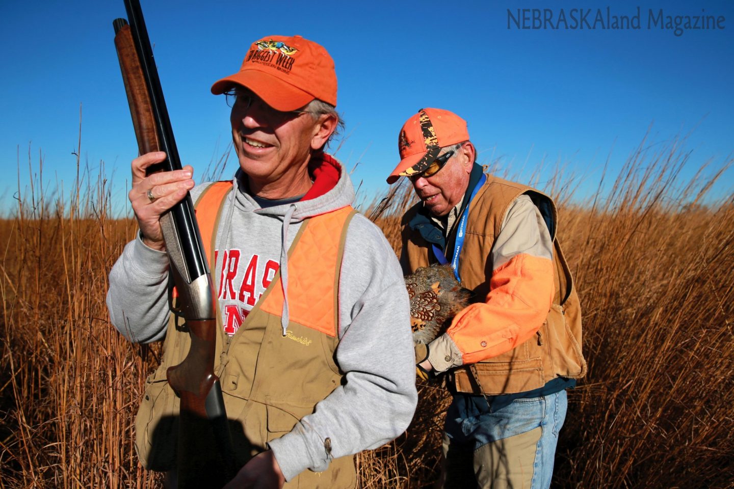 A man placing a rooster pheasant in the vest of another hunter.