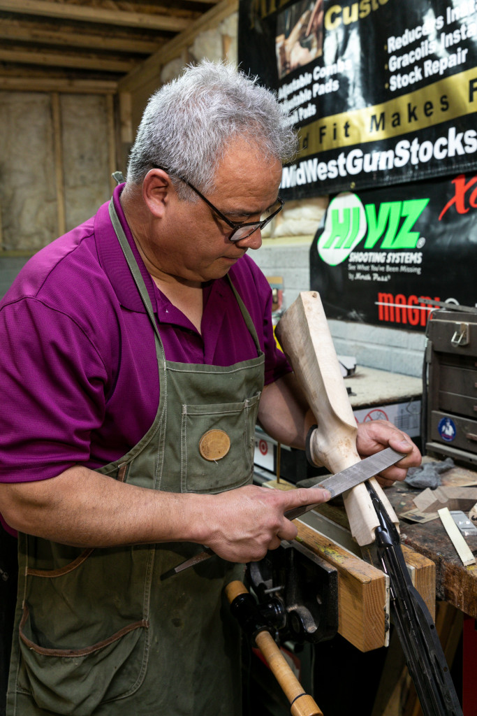 A gunsmith smoothing down a wooden gunstock.