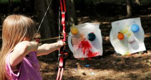 Little girl shooting arrows at paint-filled balloons