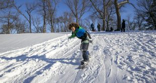 A teenage boy snowboards down a large hill.