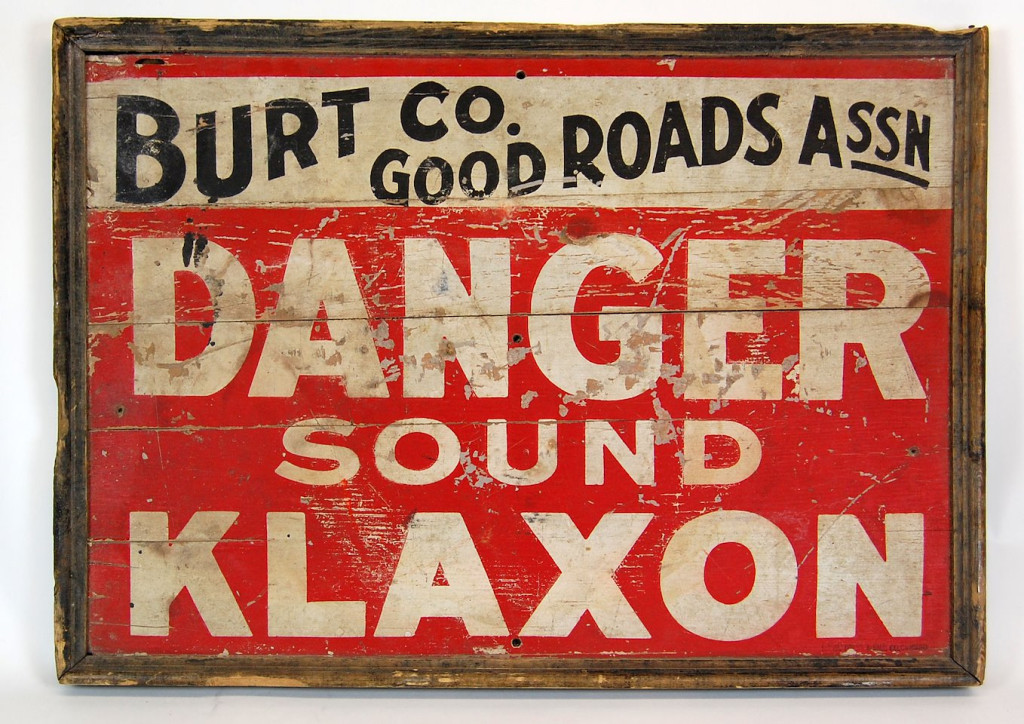 A red road sign that reads: Burt Co. Good Roads Assn. Danger Sound Klaxon