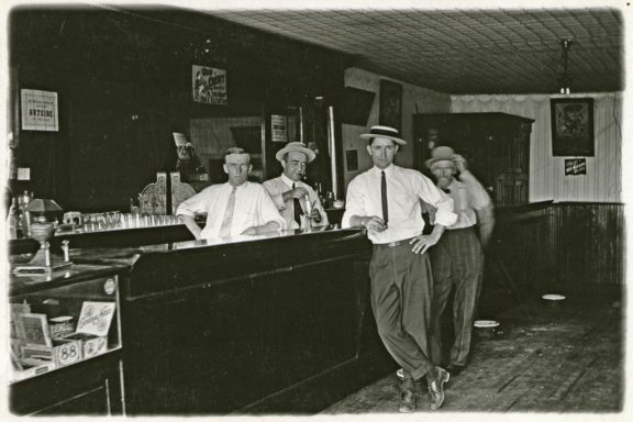 Men line up behind the bar and in front of it with smug smiles for a photograph