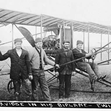 Three men sit on the wings of one of the first planes