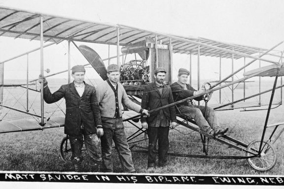 Three men sit on the wings of one of the first planes