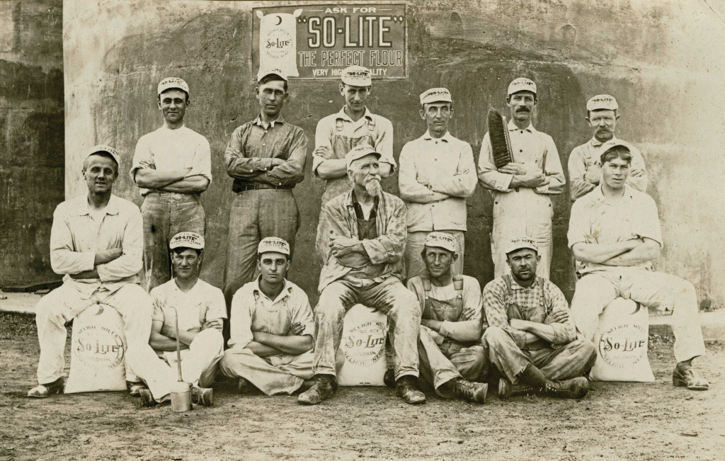 Two rows of men in white uniforms and white hats pose for a photo