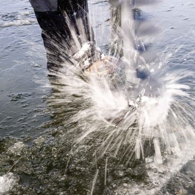 Water splashes upward as a auger is used to cut a hole in the ice of a pond