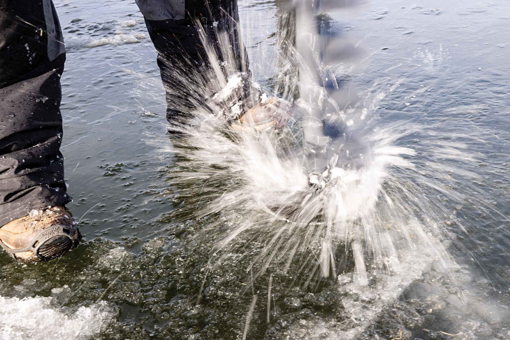 Water splashes upward as a auger is used to cut a hole in the ice of a pond