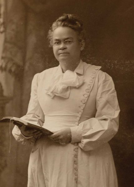 A portrait of a grim woman with spectacles in a white 1900s dress