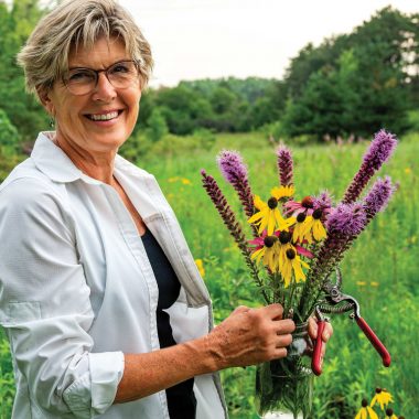 A woman poses in her backyard, which she restored into prairie.