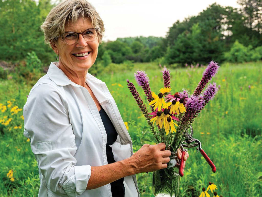 A woman poses in her backyard, which she restored into prairie.