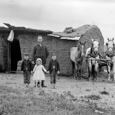 Black and white photo of a pioneering family standing in front of a sod house they built