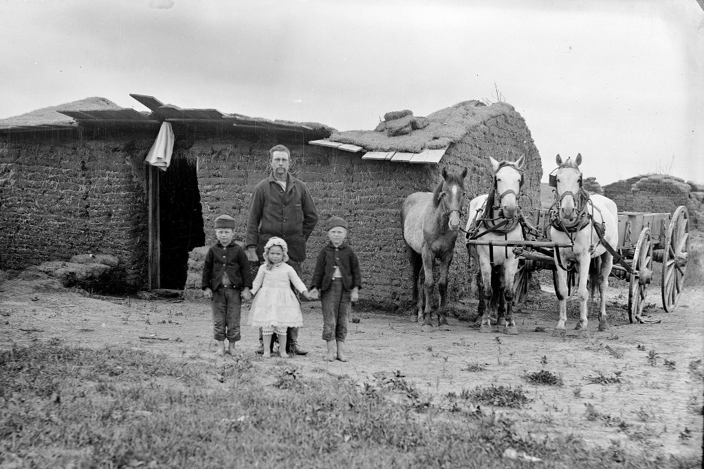 Black and white photo of a pioneering family standing in front of a sod house they built