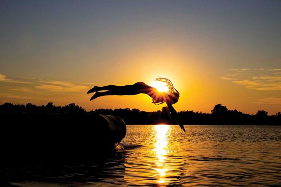 A girl dives off of a floating tube into the water at sunset.