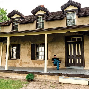 A reenactor in Union blues sits on the porch of a historic home