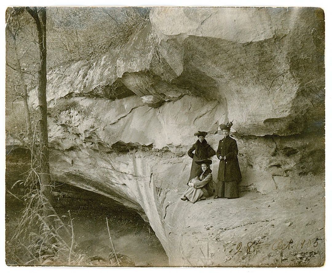 Vintage photo from 1905 of three women standing underneath ancient petroglyphs at Indian Cave State Park.