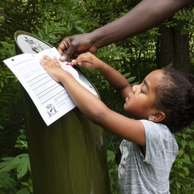 A young girl creates a rub at a Great Park Pursuit post.