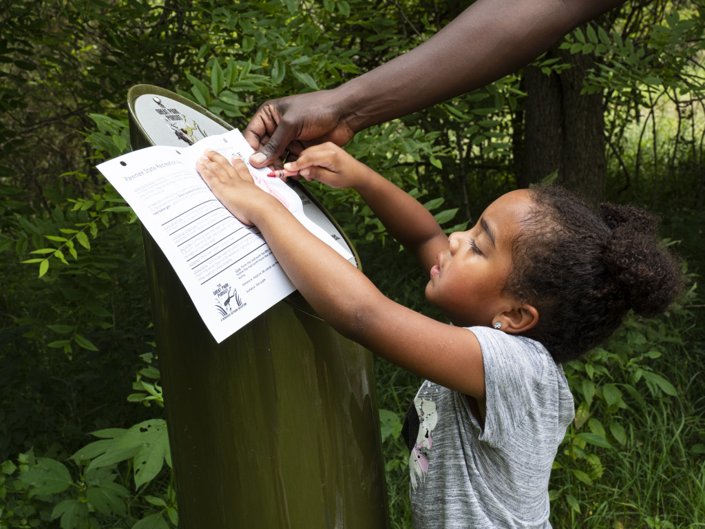 A young girl creates a rub at a Great Park Pursuit post.