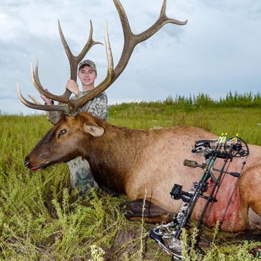 A 21-year-old male archery hunter poses with a male elk that he shot.