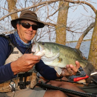 A man holds a large bass he caught while kayak fishing during summer.