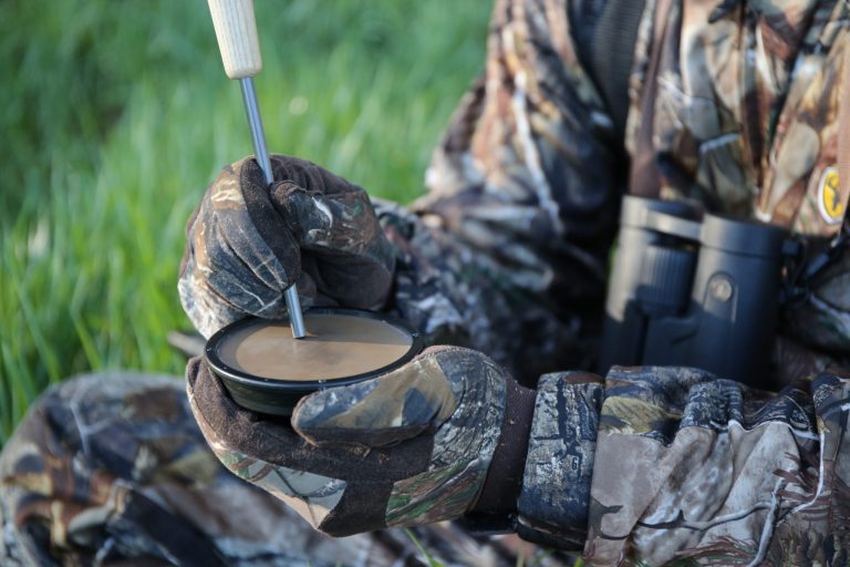 A hunter wearing camo uses a turkey call.