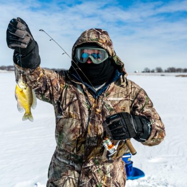 A man ice fishing and holding up a bluegill.