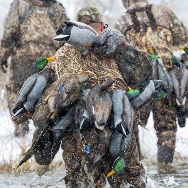 Waterfowl hunters crossing water in winter during snowfall.