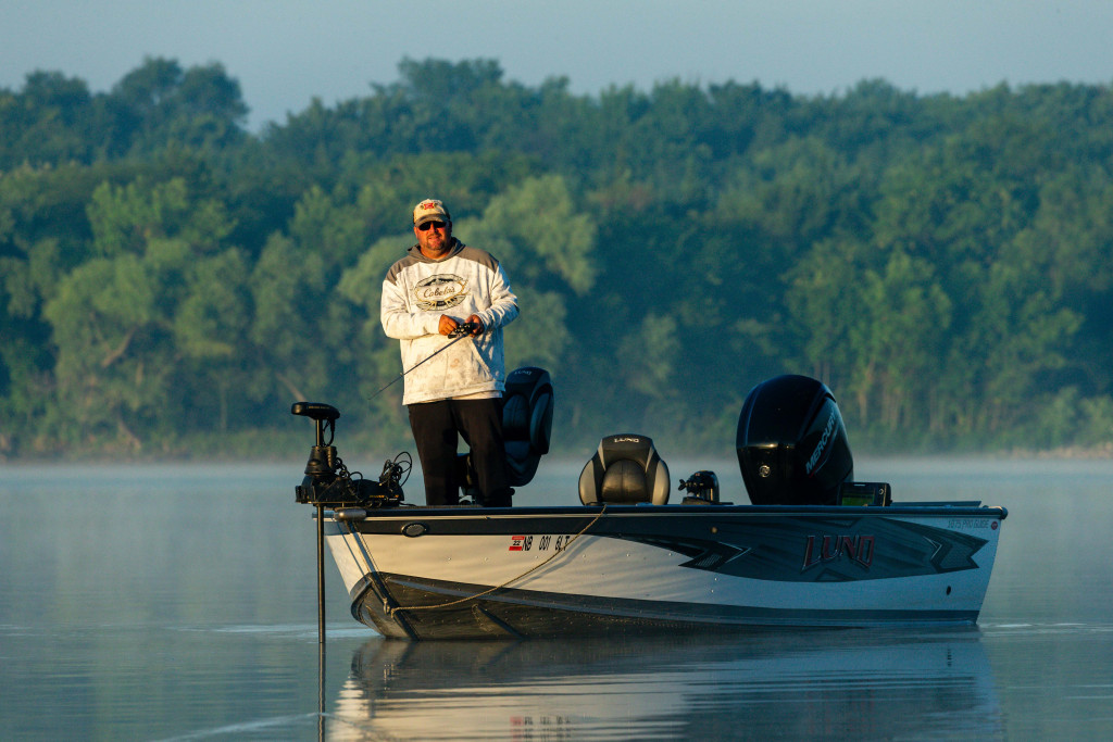 A man stands in a fishing boat, reeling in his line