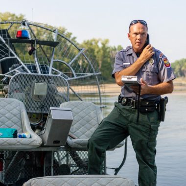 A male conservation officer makes a call to background check two men on the river.