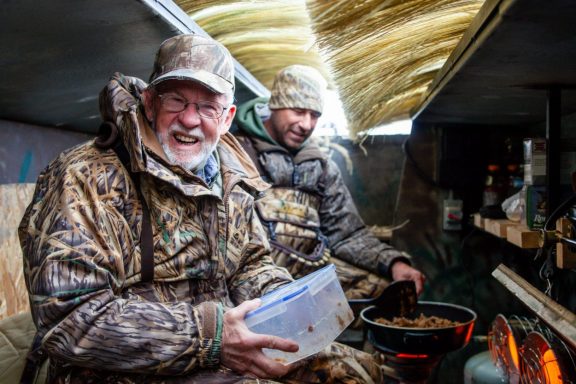 Two men cooking breakfast in a pit duck blind.