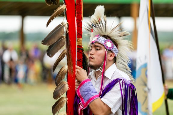 A male powwow dancer holding the Ponca eagle staff during Grand Entry.