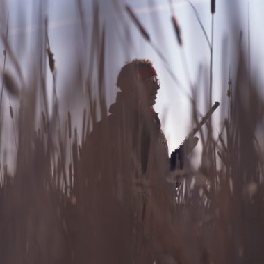 A silhouetted upland hunter walks through tallgrass prairie.