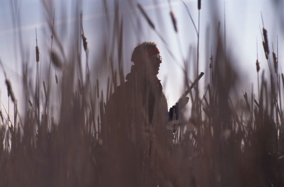 A silhouetted upland hunter walks through tallgrass prairie.