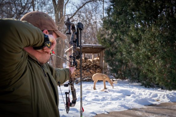 A man aims at a foam deer with a bow while practicing archery hunting.