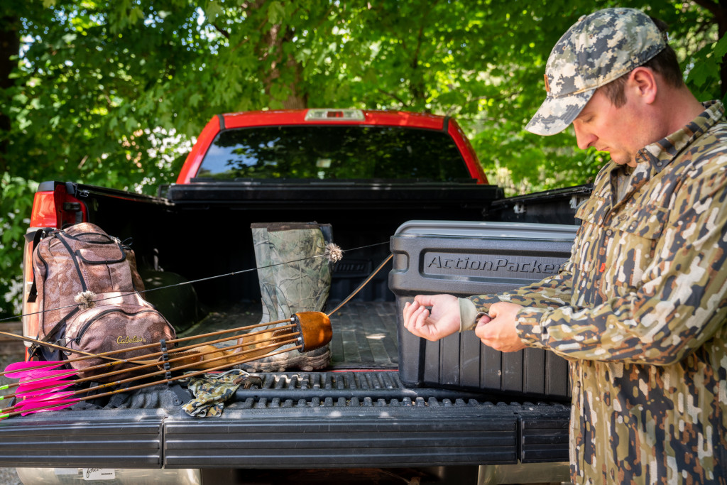 A hunter puts gear he is not wearing in the back of his truck bed.