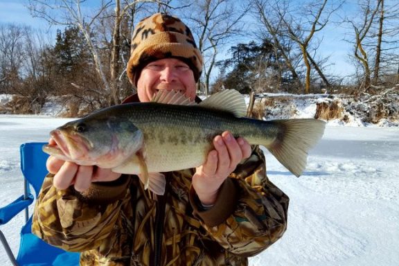 A man holds up a largemouth bass caught while ice fishing in Nebraska.