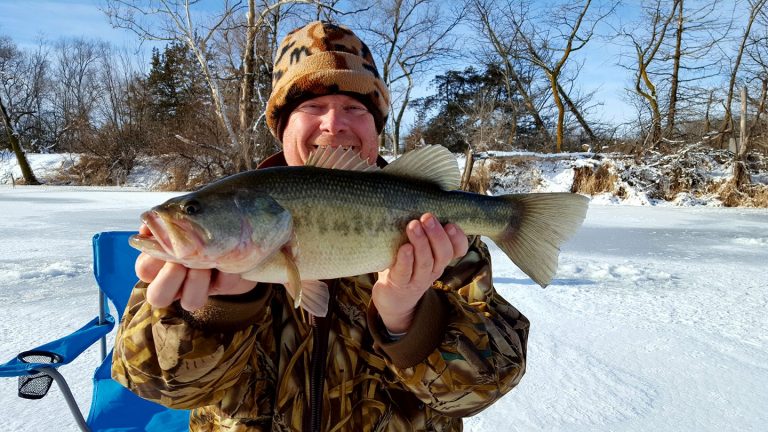 A man holds up a largemouth bass caught while ice fishing in Nebraska.