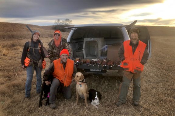 A family poses with harvested pheasants and hunting dog on CRP land in Nebraska.