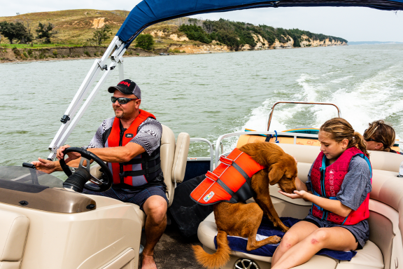 A family and their dog boating on a lake wearing life jackets.