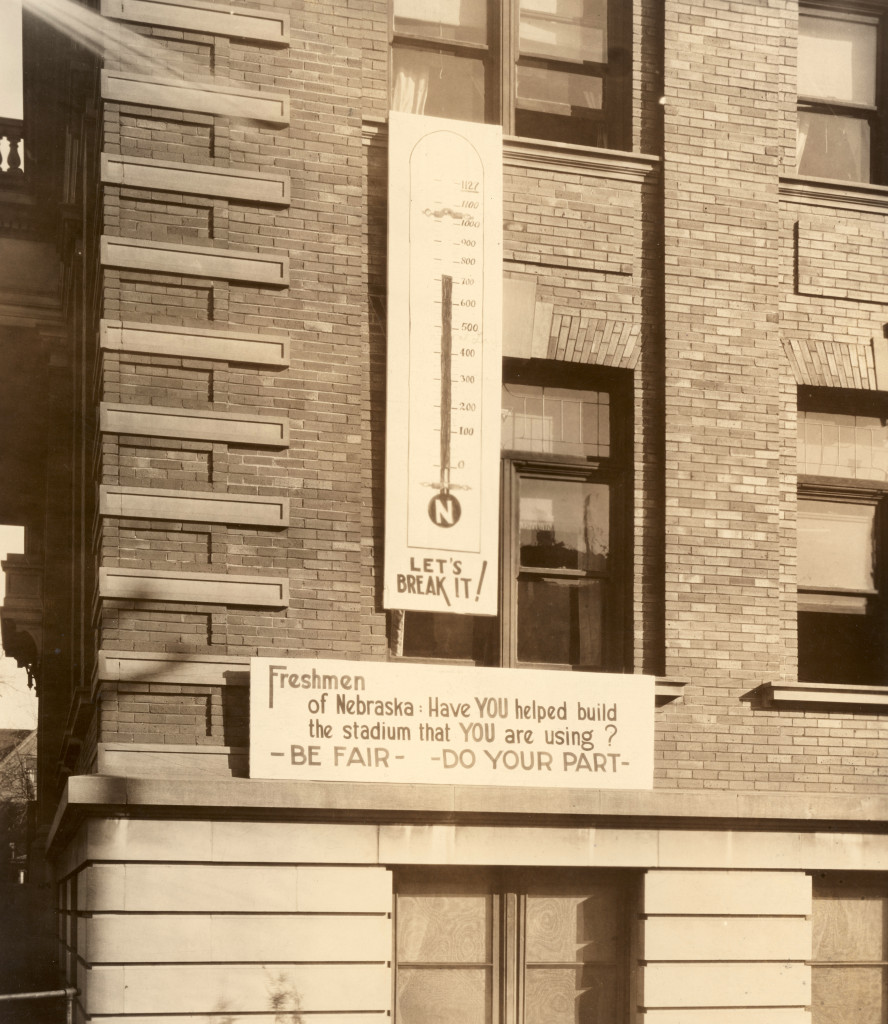 A close-up shot of a sign on a brick building asking "Have You Helped Build the Stadium you are using? Be fair. Do your part."