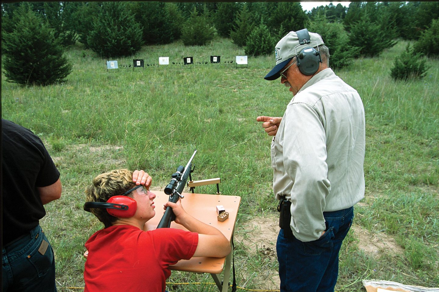 A male hunter ed instructor teaching a boy to shoot at the shooting range.