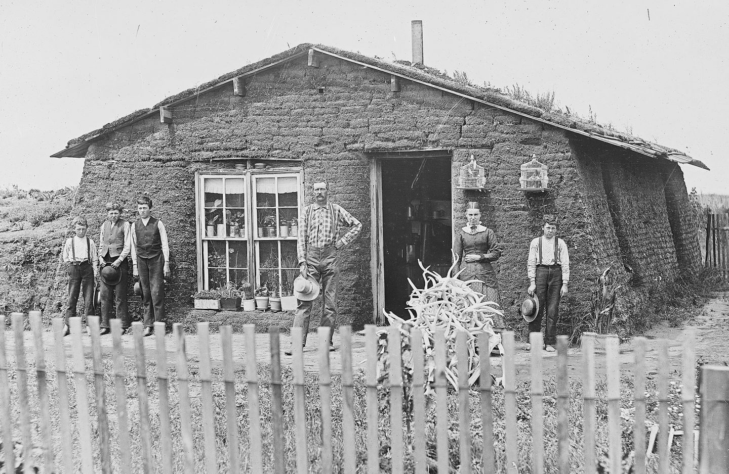 A family in front of a sod house with a fence around it.