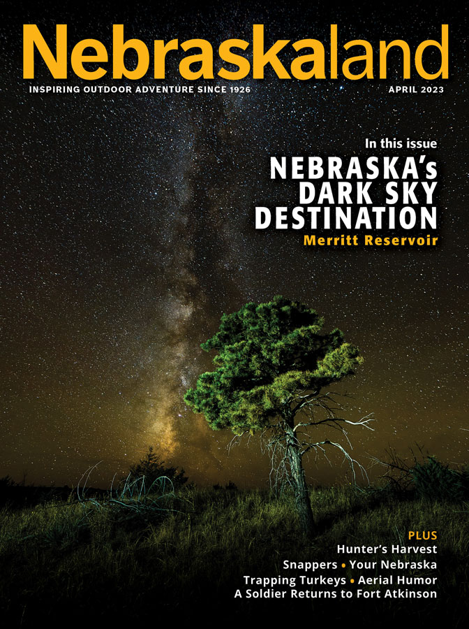 April 2023 Nebraskaland Magazine cover featuring the milky way shining above a tree at Merritt Reservoir SRA.