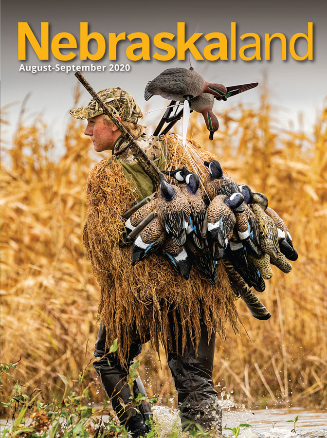 August-September cover of Nebraskaland featuring a duck hunter carrying decoys in a wetland.