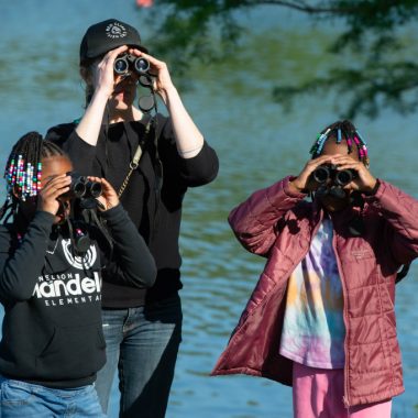 a woman and two girls hold binoculars to their faces