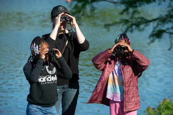 a woman and two girls hold binoculars to their faces