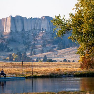 A couple fishes at Grabel Ponds at Fort Robinson State Park during fall with Red Cloud Buttes in the distance.