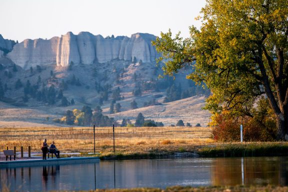 A couple fishes at Grabel Ponds at Fort Robinson State Park during fall with Red Cloud Buttes in the distance.