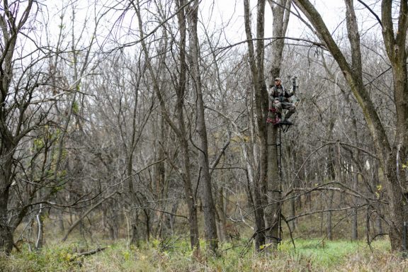 A hunter sits in a deer tree stand in a forest.